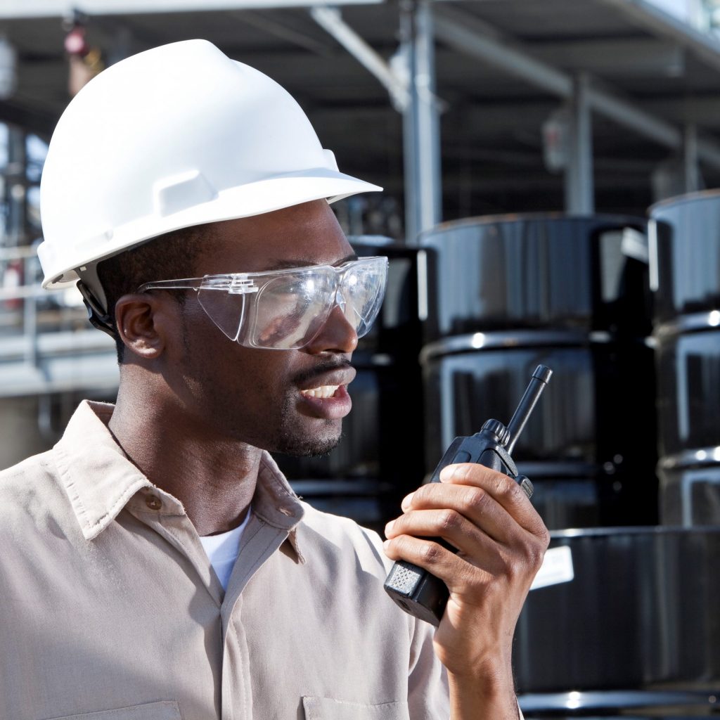 Young African American worker speaking into walkie-talkie, at chemical plant