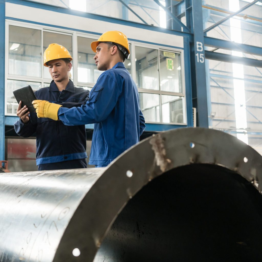 Asian experts checking information on tablet PC while supervising work in a modern factory