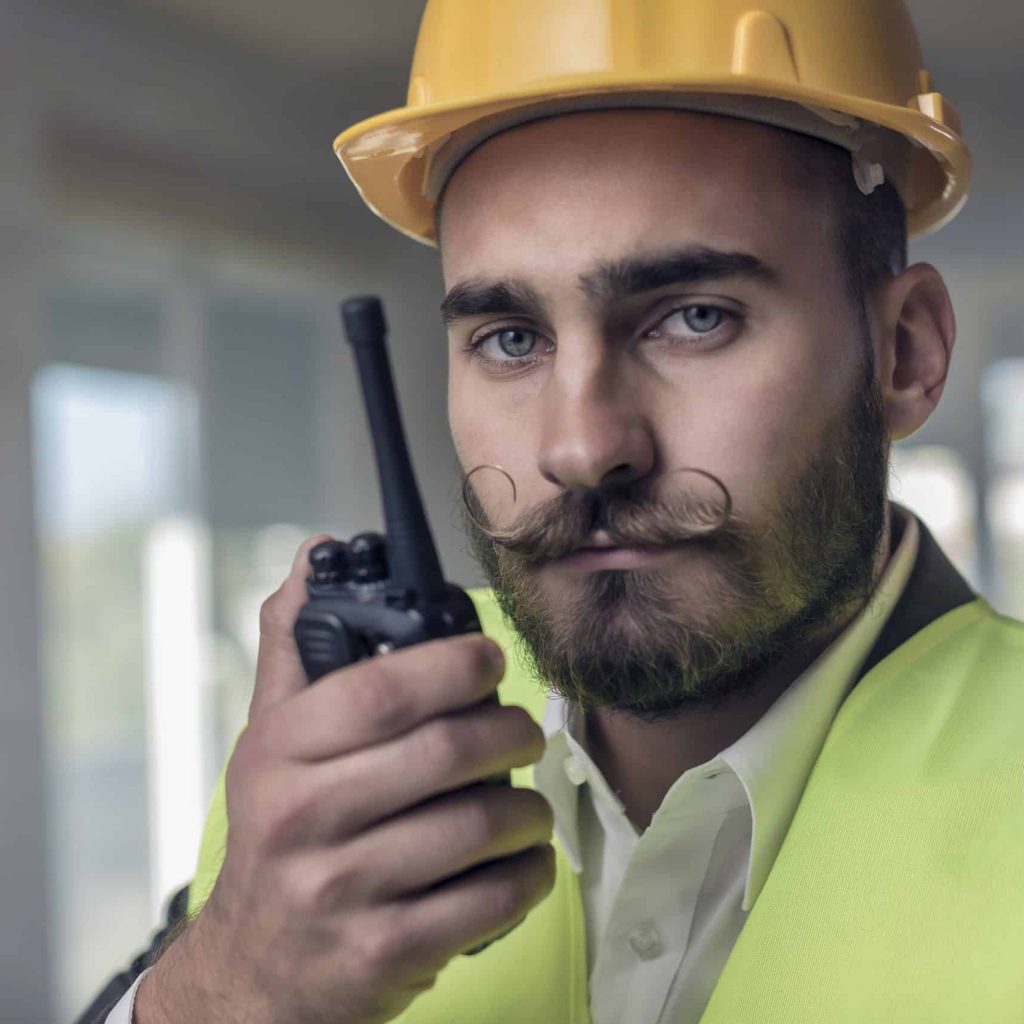 Young hipster constructor using a two way radio at the construction site.