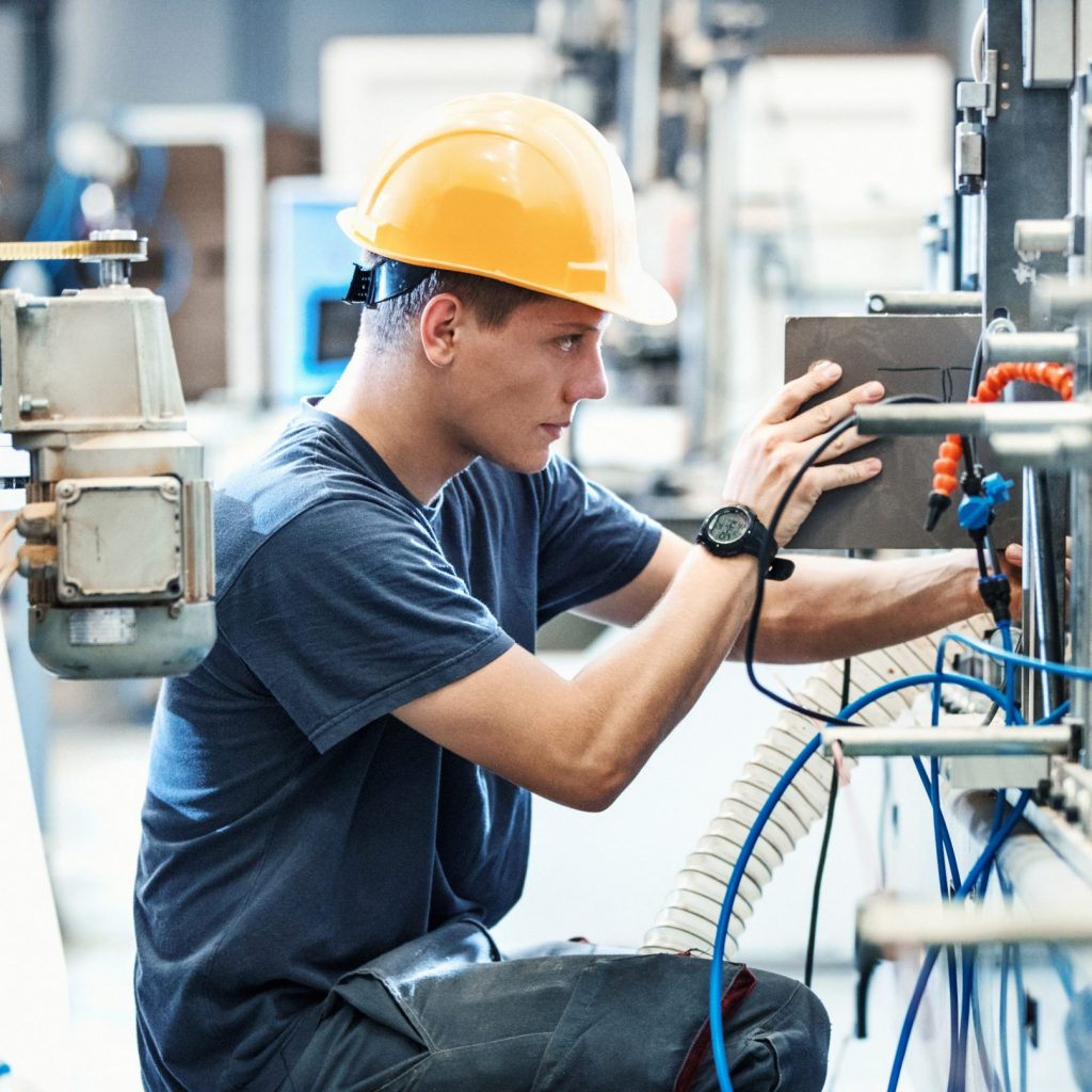 Closeup side view of  early 30's male employee at a factory plant operating a production line machine and setting it for work. It's typical work day at a factory.