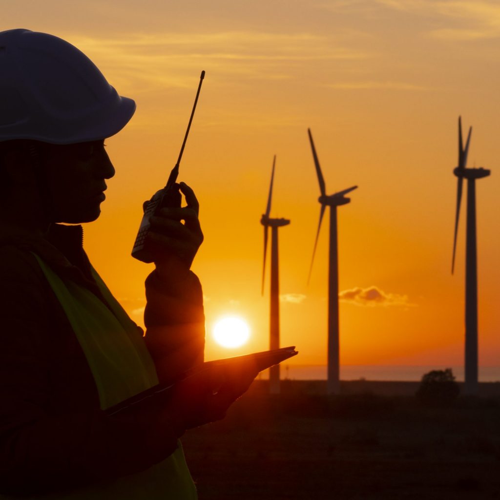 Electrical engineer working for the energy industry, supervising the condition of the Electrical Power Equipment in a wind turbines farm power station at night. Checking the data and the results of measurements with digital tablet and communicationg with the rest of the team. Technology and Global Business.