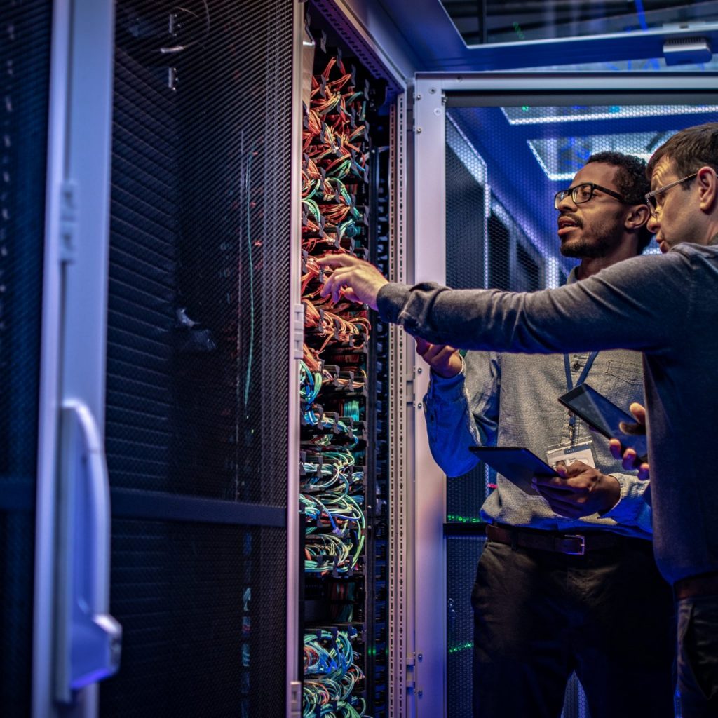 Two male IT engineers checking servers in server room with help of tablet.