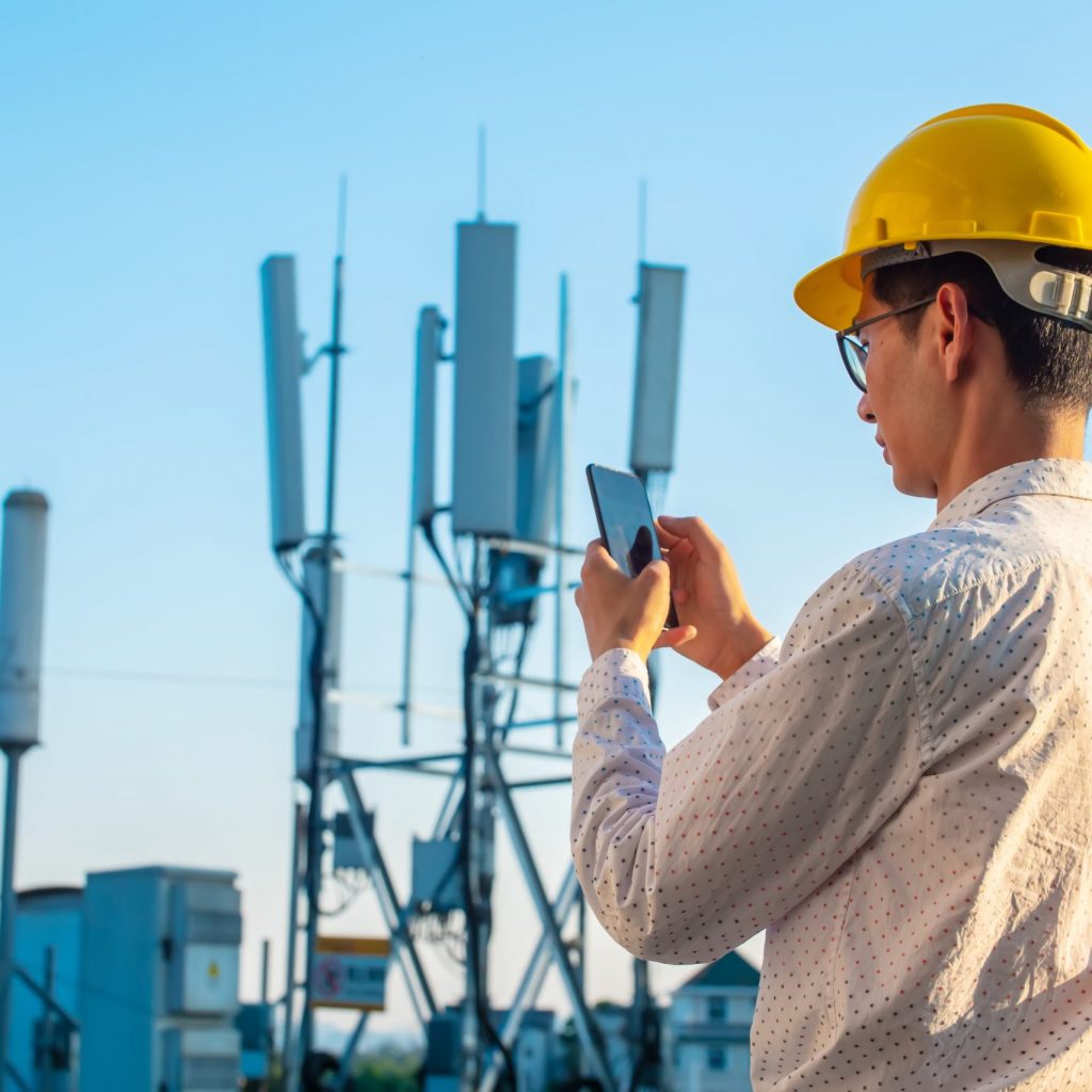 Engineer holding mobile phone testing the communications tower