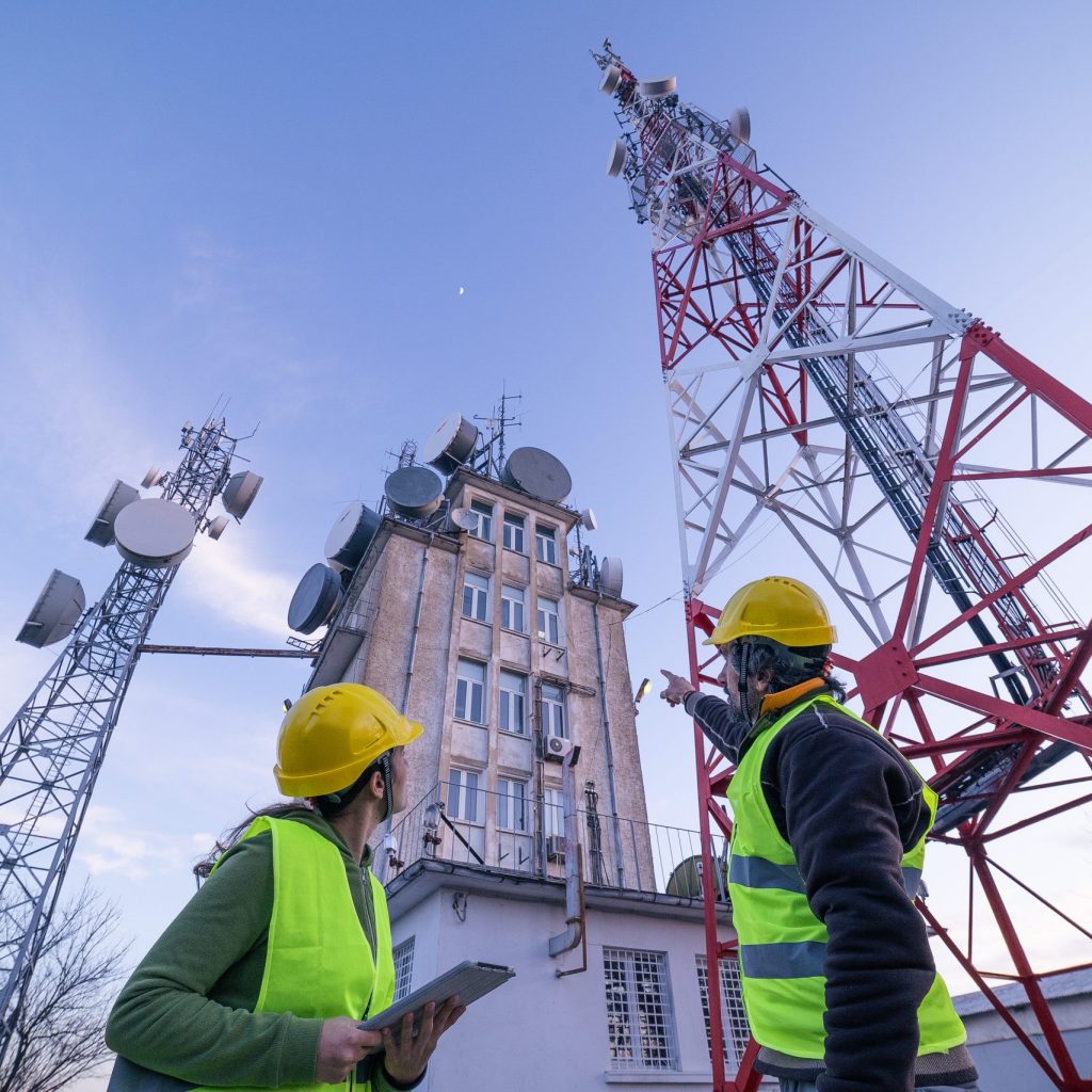 Wireless Solutions in Alberta Engineers working on the field near a city Telecommunications tower, checking the condition of the Equipement. Technology and Global Business.