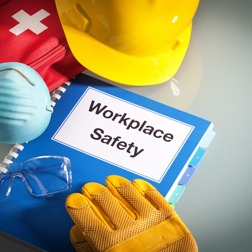 Workplace safety handbook with occupational safety equipment still life, a work training class and instruction manual for using safety equipment and administering first aid. Employment education document with protective eyewear, hard hat, first aid kit, work glove, and pollution mask. Guidance and planning tools in horizontal format with copy space.